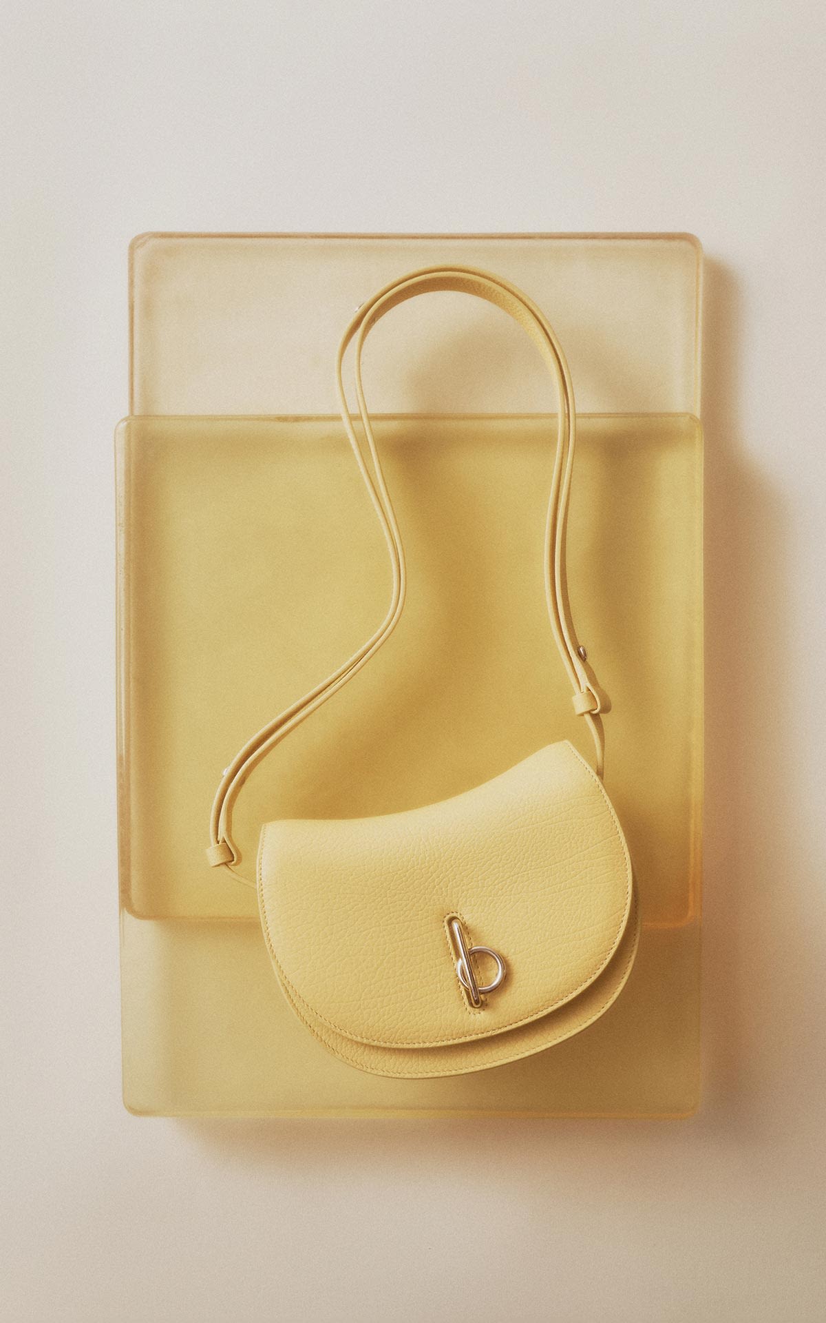 Burberry women's small pale yellow leather shoulder bag with a silver logo clasp as part of The Amber Room editorial at Bicester Village