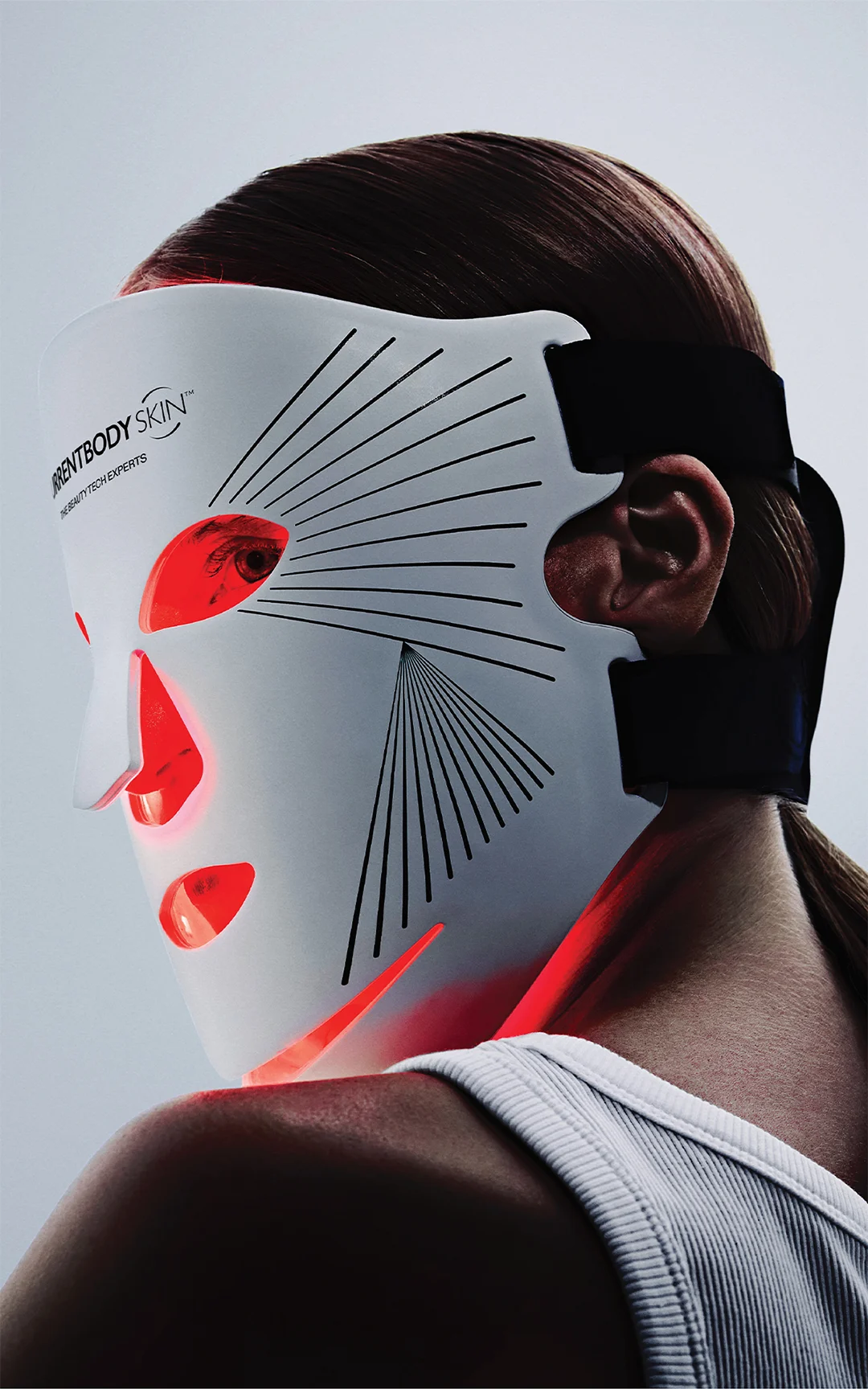 Side profile of a person wearing a white LED facial mask with red glowing eye, mouth and chin openings and black strap.